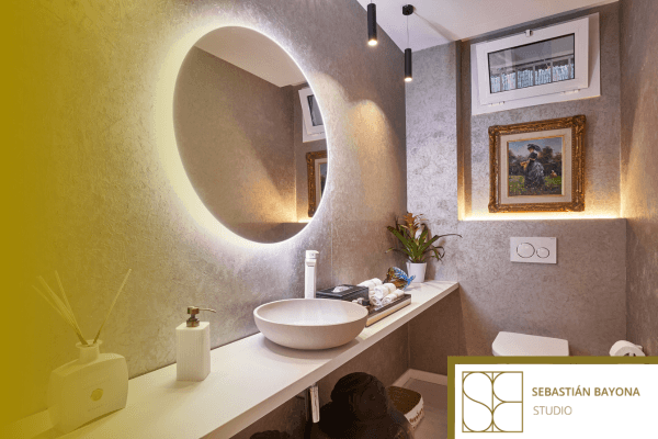 Baño contemporáneo con espejo redondo retroiluminado lavabo sobre encimera y paredes en tonos piedra